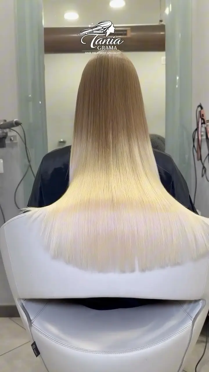 Il salone in Via Tolemaide: una cliente di spalle con i capelli biondi lisci, sopra lo specchio il logo Tania Grama